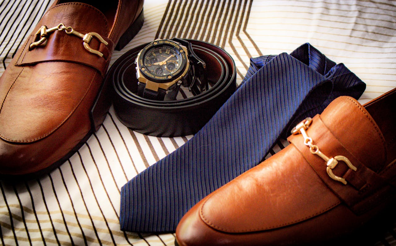 cta-01 Close-up of elegant leather shoes, wristwatch, belt, and tie on striped fabric. Perfect for men's fashion.